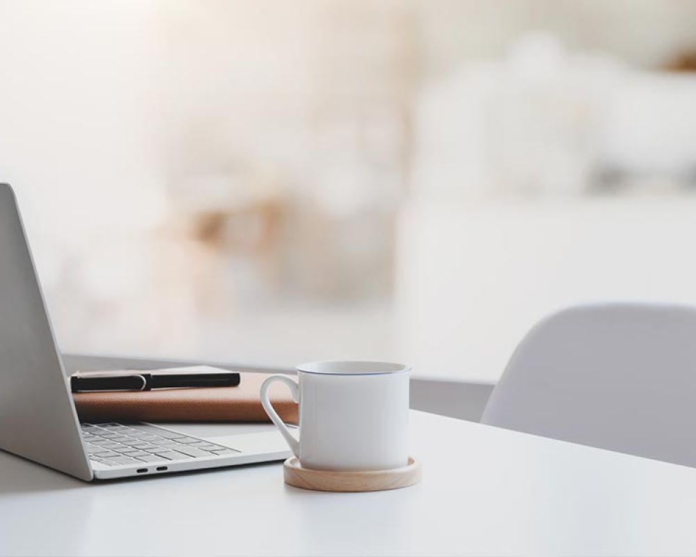 Laptop, Tasse und Notizbuch auf einem Schreibtisch, symbolisiert einen modernen Arbeitsplatz in einer Marketingagentur. Laptop, Tasse und Notizbuch auf einem Schreibtisch, symbolisiert einen modernen Arbeitsplatz in einer Marketingagentur.