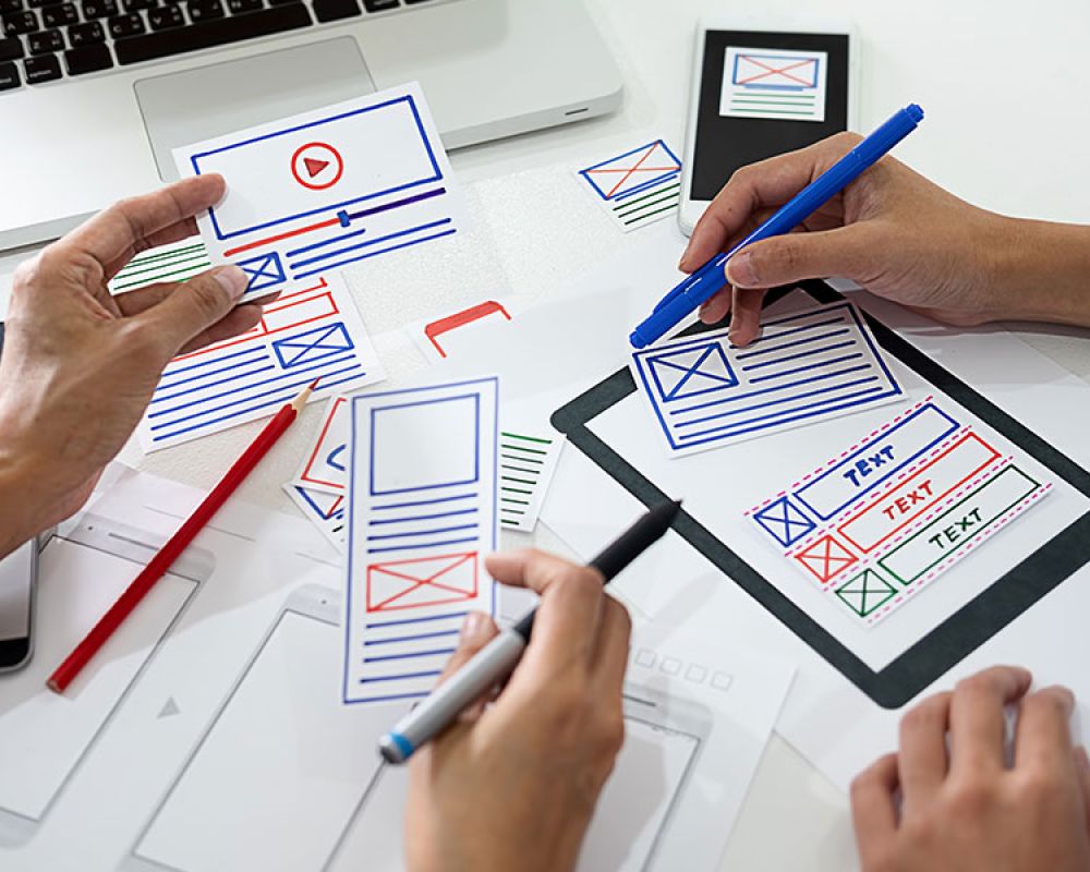 Zwei Personen arbeiten an einem Webdesign-Plan mit handgezeichneten Layouts und Markierungen, verdeutlicht die Bedeutung von strategischem Webdesign in einer Marketingagentur.