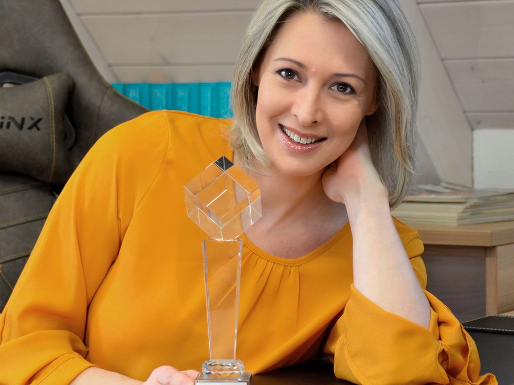 Frau in gelber Bluse lächelt und hält eine Trophäe, die ihren Erfolg und ihre Auszeichnung hervorhebt.