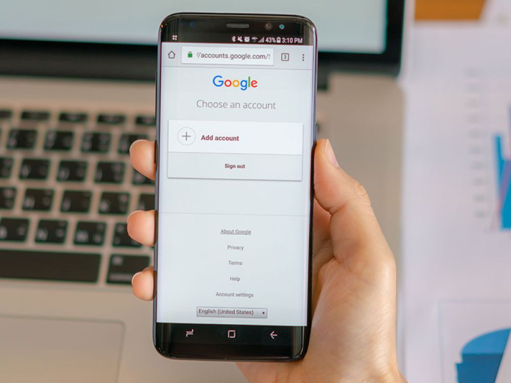Smartphone mit Google-Anmeldebildschirm vor einem Laptop, repräsentiert die Nutzung von Google-Diensten auf mobilen Geräten.