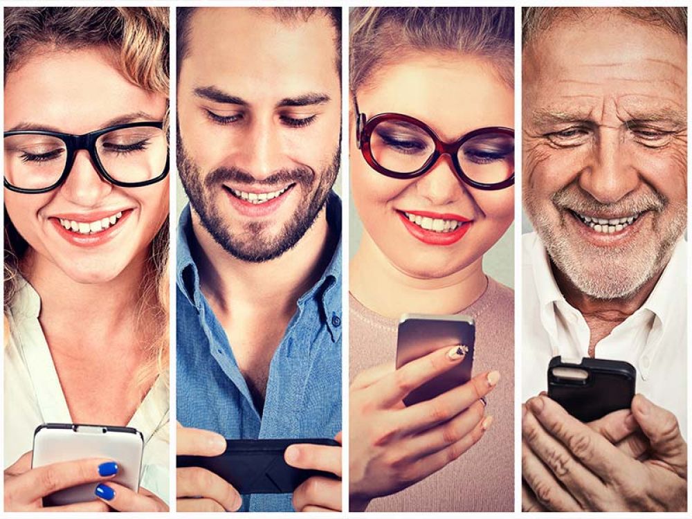 Vier Personen unterschiedlichen Alters und Geschlechts, die lächelnd auf ihre Smartphones schauen, symbolisieren die Zielgruppenansprache und Nutzerinteraktion im digitalen Marketing.
