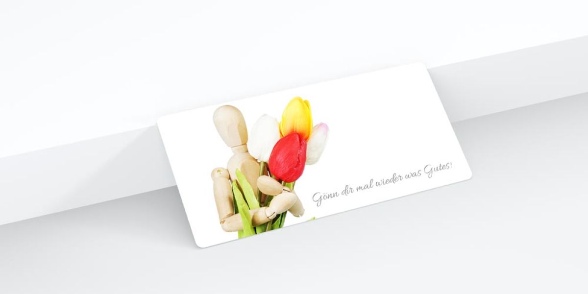 Geschenkgutschein der Naturheilpraxis Fürstenfeldbruck mit einer Holzfigur und Tulpen, gestaltet von unserer Werbeagentur.