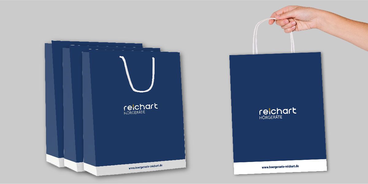 Blaue Einkaufstaschen mit dem Logo von Hörgeräte Reichart, entworfen von getaweb für Merchandise-Produkte, zeigen das Corporate Design und die Markenidentität.