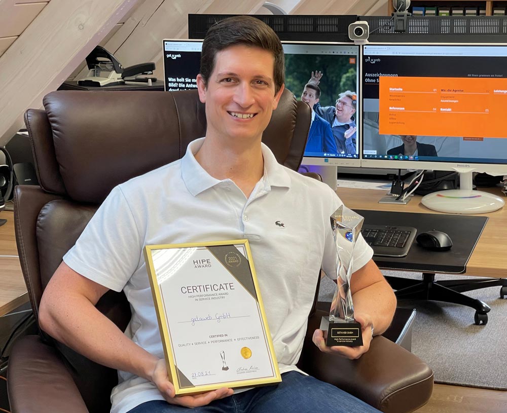 Mann in weißem Polohemd lächelt und hält eine Trophäe sowie ein Zertifikat für den High Performance Award, das seine Auszeichnung und Erfolg zeigt. Mann in weißem Polohemd lächelt und hält eine Trophäe sowie ein Zertifikat für den High Performance Award, das seine Auszeichnung und Erfolg zeigt.